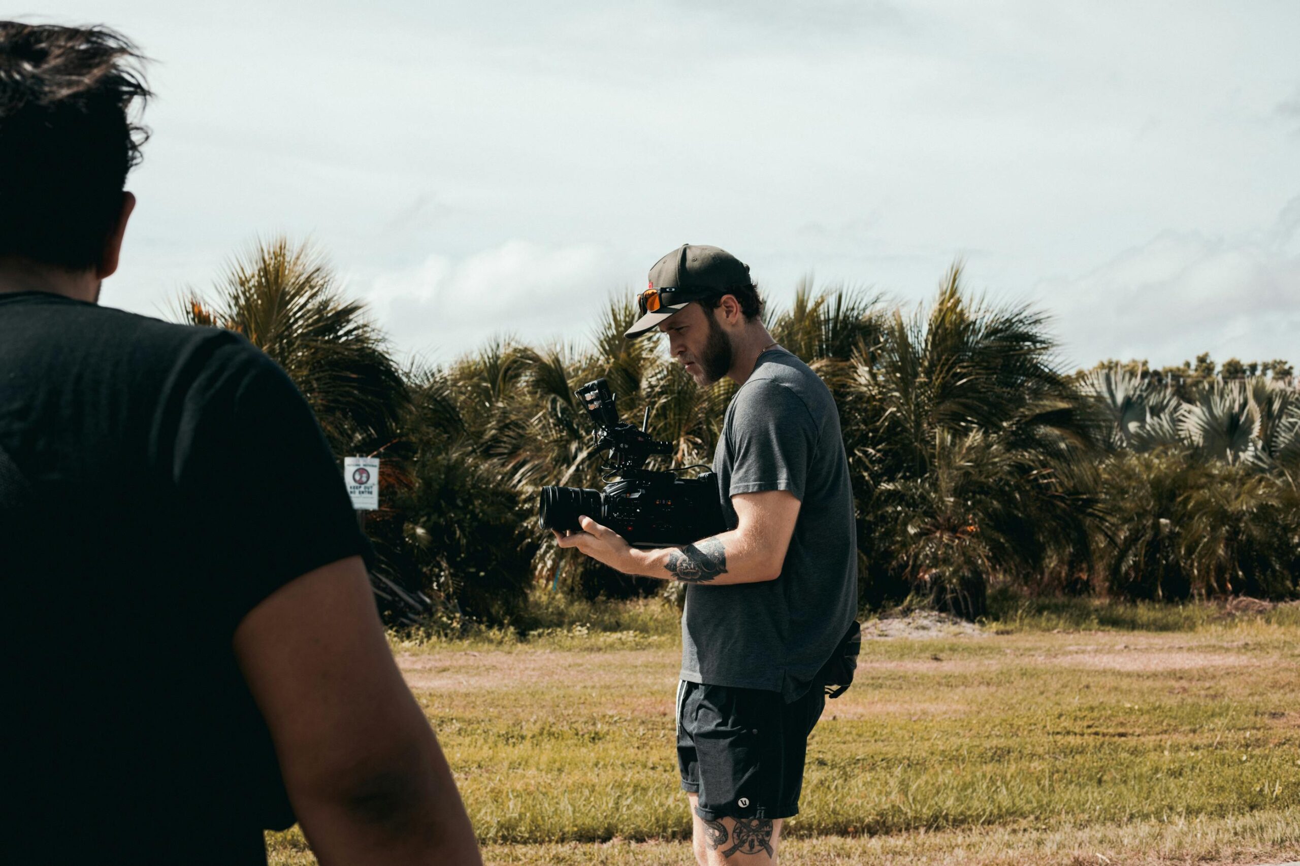 Man in Grey T-shirt and Black Shorts Standing on Green Grass Field While Holding a Camera